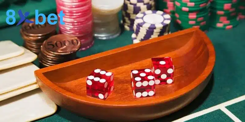 Ba viên xúc xắc đỏ trong khay gỗ trên bàn casino cùng nhiều chồng chip