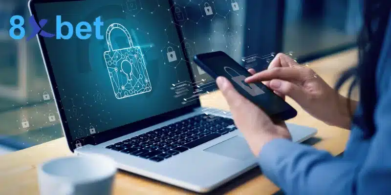Người dùng cầm điện thoại bên laptop hiển thị biểu tượng ổ khóa khi đăng nhập 8xbet