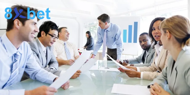 Nhóm nhân sự văn phòng họp quanh bàn kính với biểu đồ cột phía sau